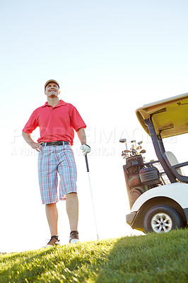 Buy stock photo A handsome man standing with his golf cart and holding his golf club with the sun setting in the background