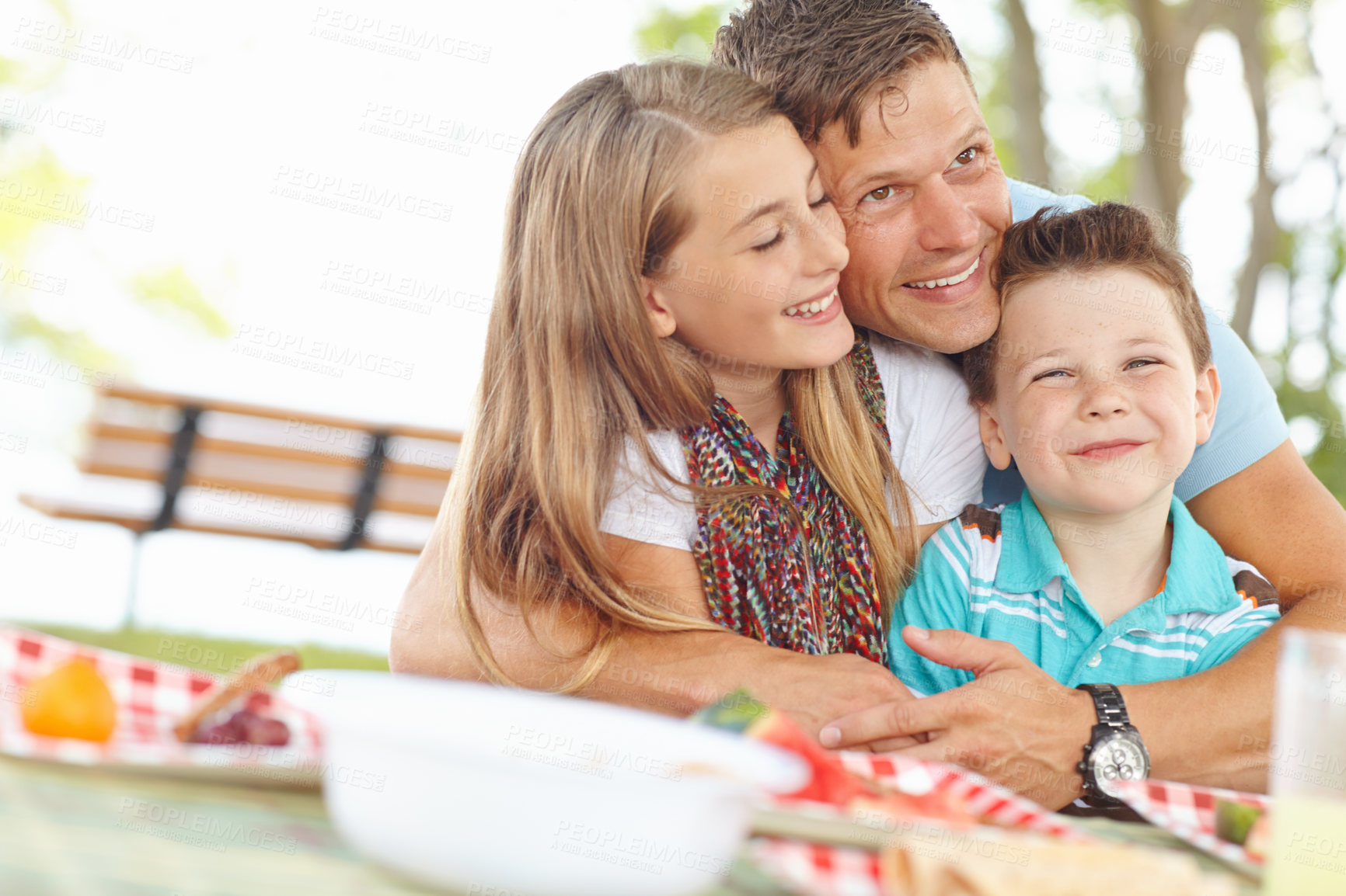 Buy stock photo Father hugging his daughter and son at the picnic table