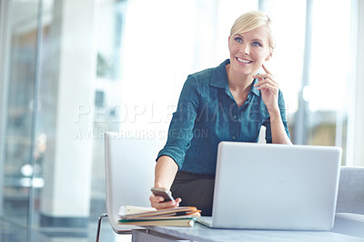 Buy stock photo Shot of a casual business woman sitting behind her laptop checking her phone with copyspace