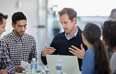 Buy stock photo Group of colleagues sitting round a meeting table having a serious discussion