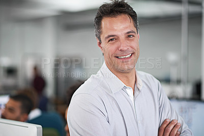 Buy stock photo Cropped shot of a handsome businessman sitting on his desk with a few colleagues in the background