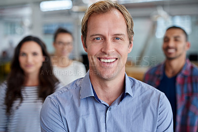 Buy stock photo Handsome man smiling at the camera with staff in the background