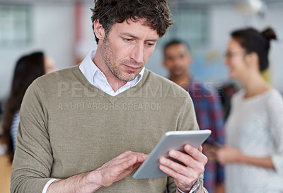 Buy stock photo Handsome mature man using a digital tablet with staff in the background