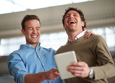 Buy stock photo Male coworkers laughing out loud about something humorous on a digital tablet in their office