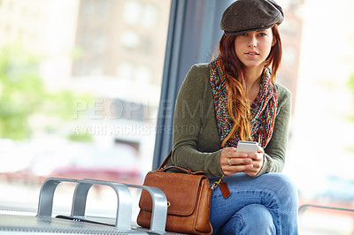 Buy stock photo Portrait of a stylish woman holding a cellphone while sitting at a train station with copyspace