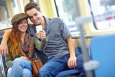 Buy stock photo A happy couple taking a picture on their phone as they sit on the train with copyspace