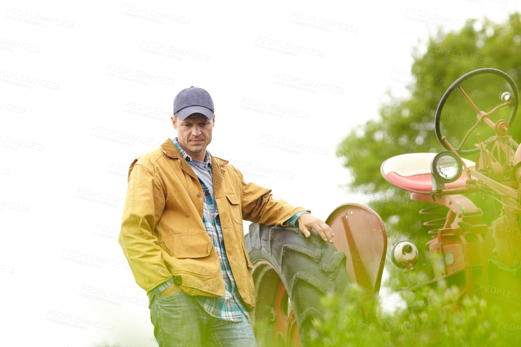 Buy stock photo Shot of a thoughtful farmer leaning against his tractor while looking down