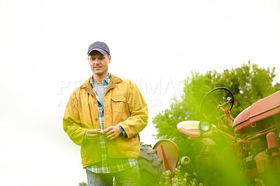 Buy stock photo Shot of a farmer standing in a field with his tractor next to him