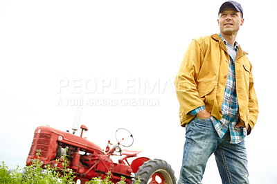 Buy stock photo Shot of a farmer standing in a field with a tractor parked behind him