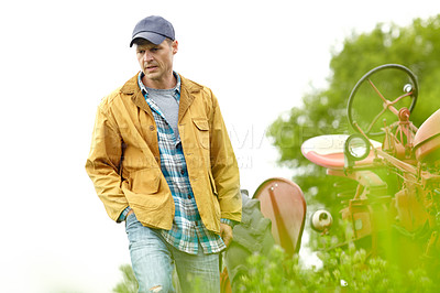 Buy stock photo Shot of a worried farmer walking away from his tractor in a field