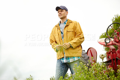 Buy stock photo Shot of a thoughtful farmer standing in a field with his tractor beside him - Copyspace