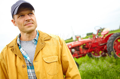 Buy stock photo A farmer standing in a field with a tractor parked behind him - Copyspace