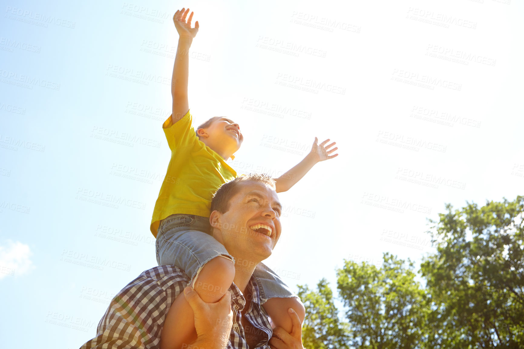 Buy stock photo Cute young boy sitting on his father's shoulders and stretching his arms up