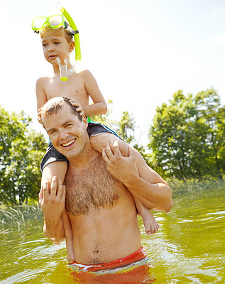 Buy stock photo Young father standing in a lake carrying his son on his shoulders and smiling