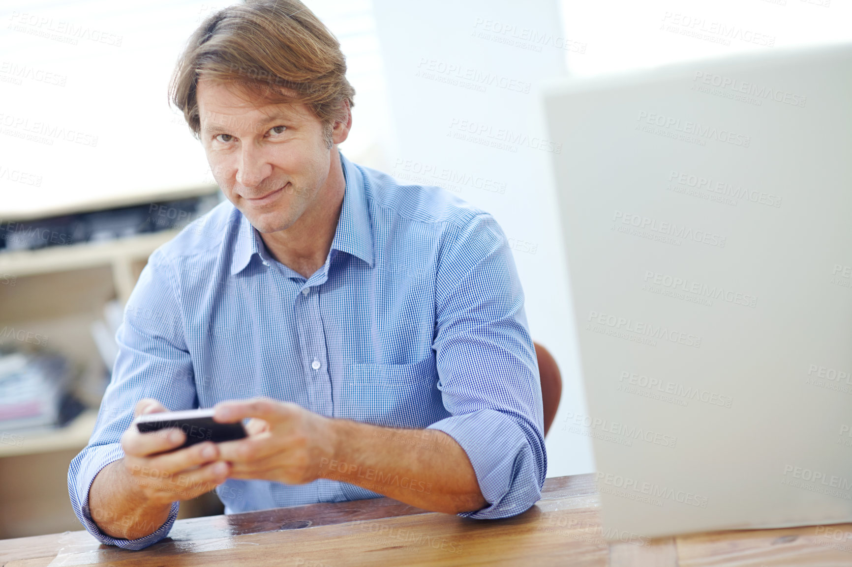 Buy stock photo Mature, attractive employee sitting and smiling slightly at an office desk while using his mobile phone