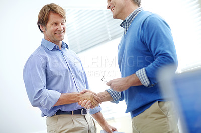 Buy stock photo Two mature, attractive businessmen shaking hands while standing in an office