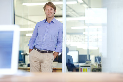 Buy stock photo Mature businessman leaning on an office doorway and smiling slightly with his hands in his pockets