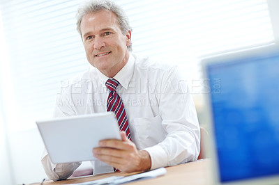 Buy stock photo Mature employee sitting at an office desk while holding a tablet