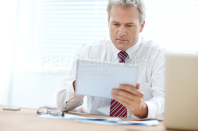 Buy stock photo Mature businessman holding a tablet while sitting at an office desk