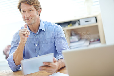 Buy stock photo Attractive businessman sitting at a desk and smiling while holding a tablet