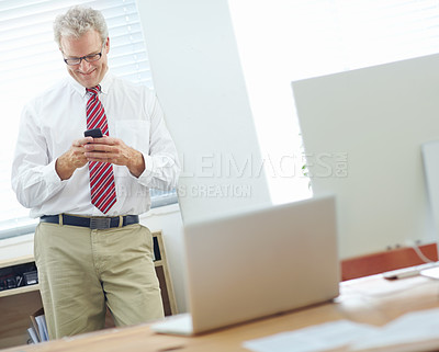 Buy stock photo Male business associate standing and leaning against the office wall while text messaging