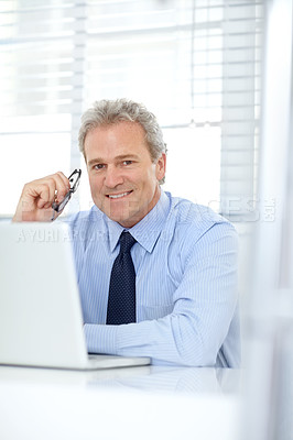 Buy stock photo Portrait of a handsome mature businessman sitting at his desk in front of a laptop