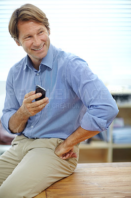 Buy stock photo Shot of a mature businessman sending a text while leaning on a table in his office