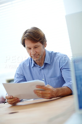 Buy stock photo Shot of a mature businessman reading paperwork while sitting at his desk