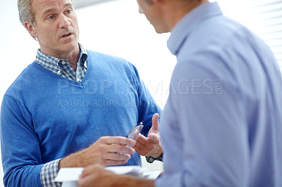 Buy stock photo Cropped shot of two mature businessmen standing in an office and discussing paperwork
