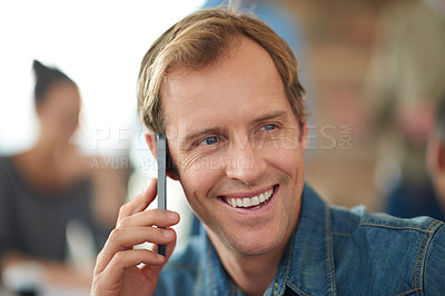 Buy stock photo Shot of a man sitting in an office talking on a cellphone with colleagues in the background