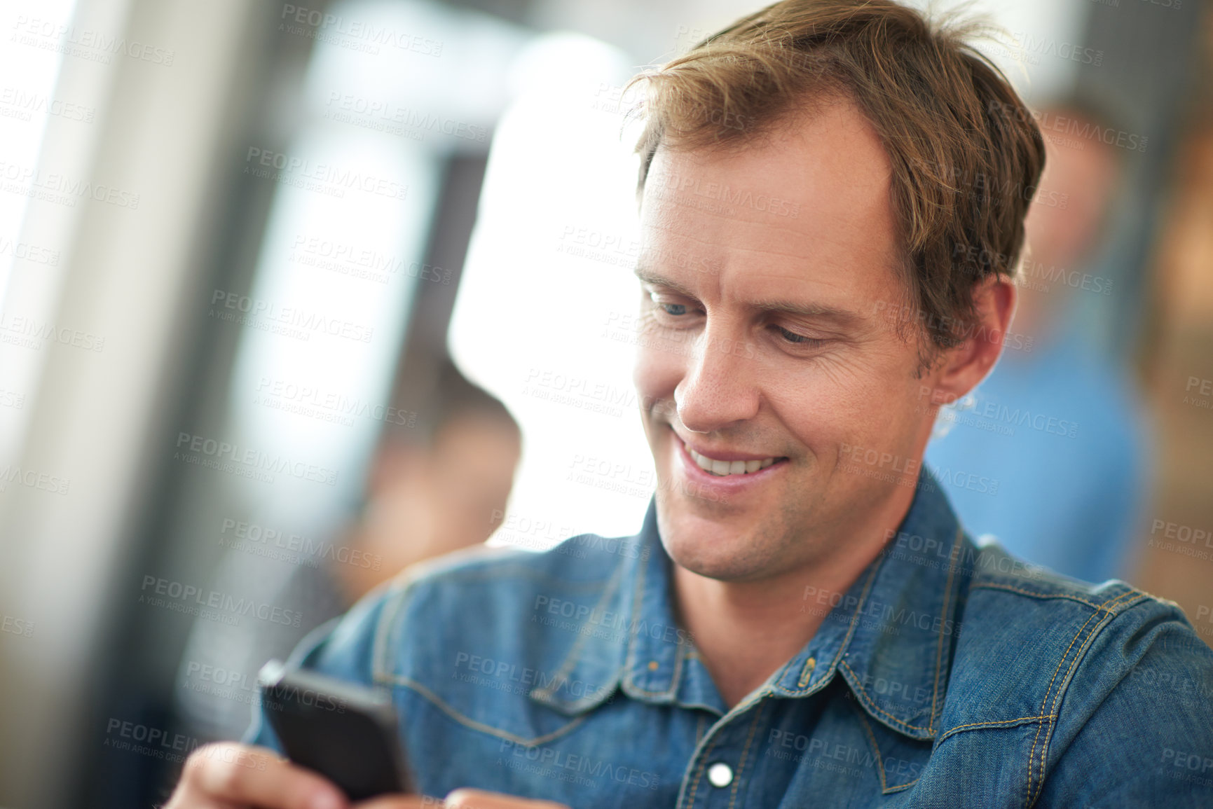 Buy stock photo Shot of a man sitting in an office messaging on a cellphone with colleagues in the background