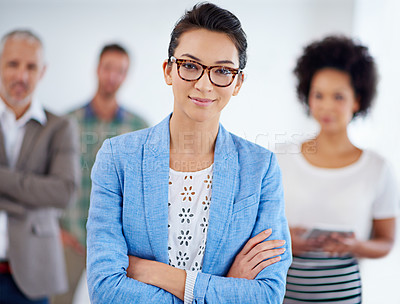 Buy stock photo Confident young businesswoman smiling at the camera with coworkers in the background