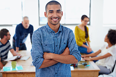 Buy stock photo Young confident businessman looking at the camera with coworkers in the background