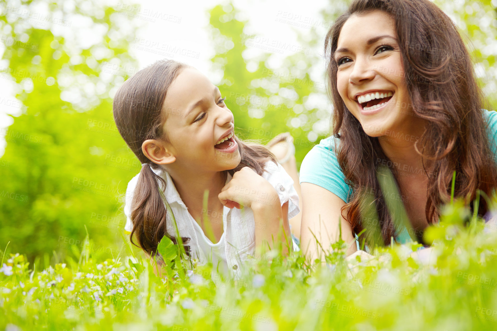 Buy stock photo A mother and daughter laughing together while lying in the grass of a meadow