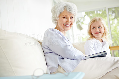 Buy stock photo Girl, elderly grandmother and book on sofa in home living room with woman, smile and story for retirement portrait. Happy, senior person and weekend for rest, family and lounge for memory on couch