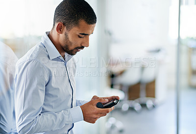 Buy stock photo Shot of a handsome young businessman using his cellphone in the office