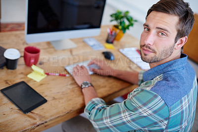 Buy stock photo Portrait of a handsome young creative sitting at his desk and looking back at you over his shoulder