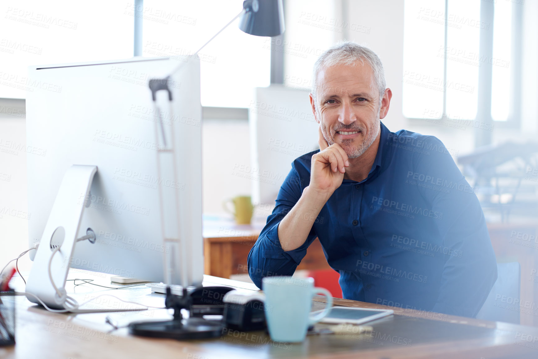 Buy stock photo Mature creative professional looking positively at the camera while sitting at his desk in a bright work space