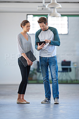 Buy stock photo Two creative professionals looking at information on a digital tablet in an open office space