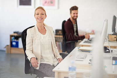 Buy stock photo Portrait of a smiling businesswoman sitting at her desk with her colleague in the background
