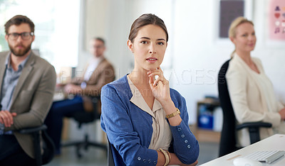 Buy stock photo Serious young businesswoman sitting at her desk with colleagues in the background
