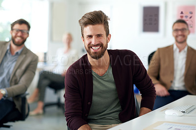 Buy stock photo Serious young professional sitting at his desk with colleagues in the background
