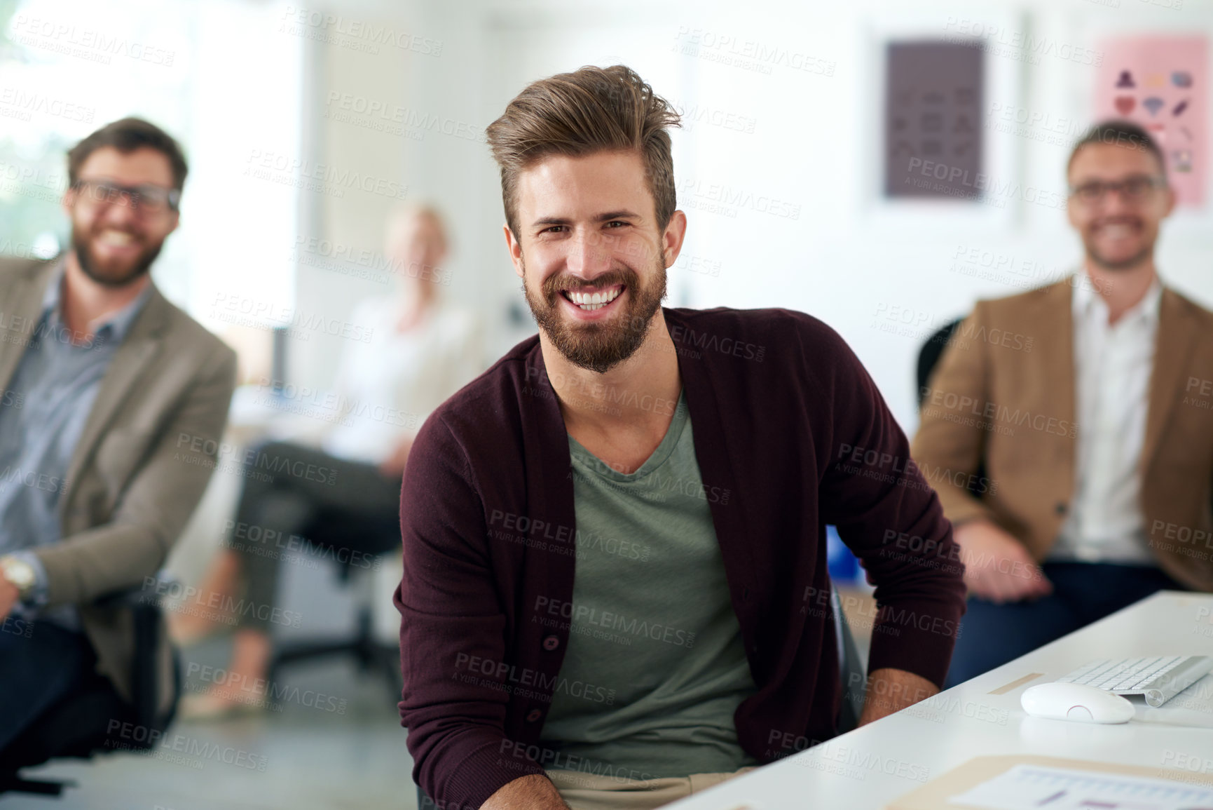 Buy stock photo Serious young professional sitting at his desk with colleagues in the background
