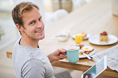 Buy stock photo Portrait of a handsome man using his tablet while having breakfast at home