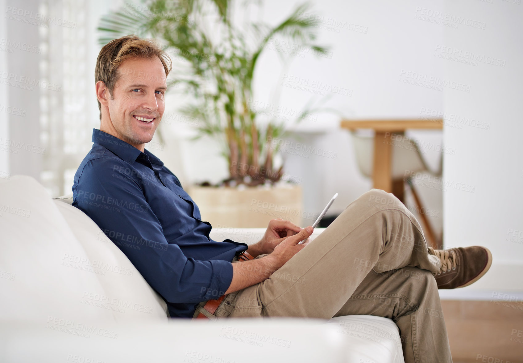 Buy stock photo Shot of a handsome man using his tablet while sitting on the sofa at home