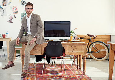 Buy stock photo Portrait of a casually-dressed young man sitting on his desk in an office