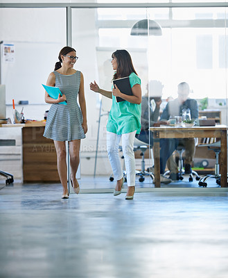 Buy stock photo Shot of a two young businesswomen talking while walking through their office