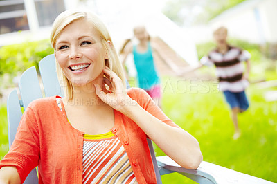 Buy stock photo Happy young mother sitting outdoors as her children play behind her