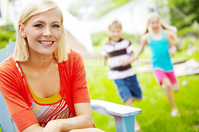 Buy stock photo Happy young mother sitting outdoors as her children play behind her