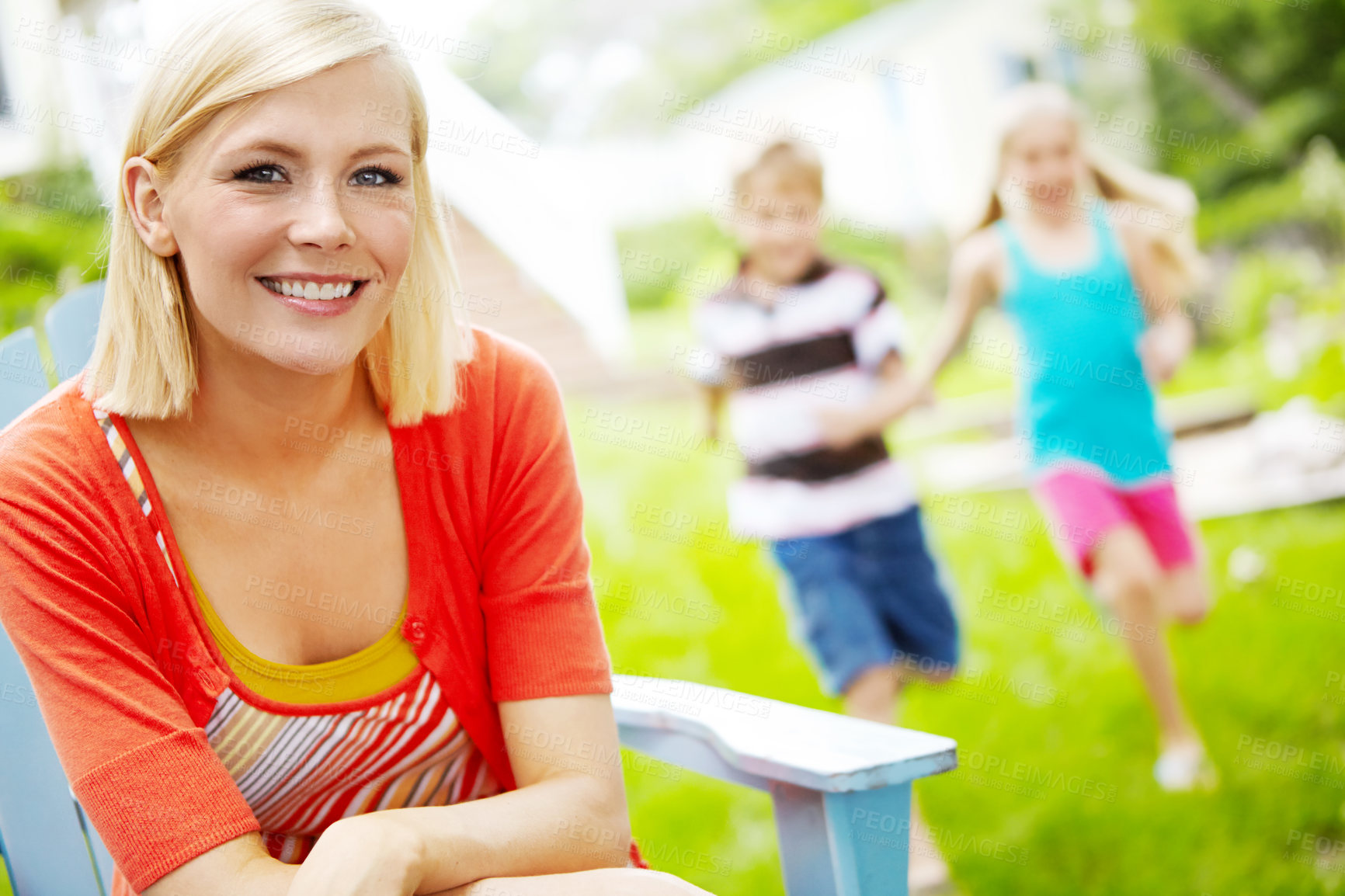 Buy stock photo Happy young mother sitting outdoors as her children play behind her